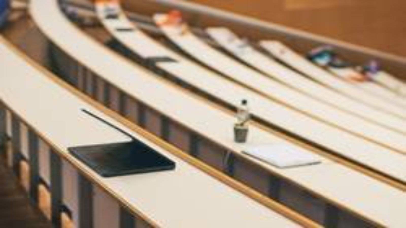 Bilde av tomme seter i et auditorium, en PC, et notatblokk og en brusflaske i forgrunnen